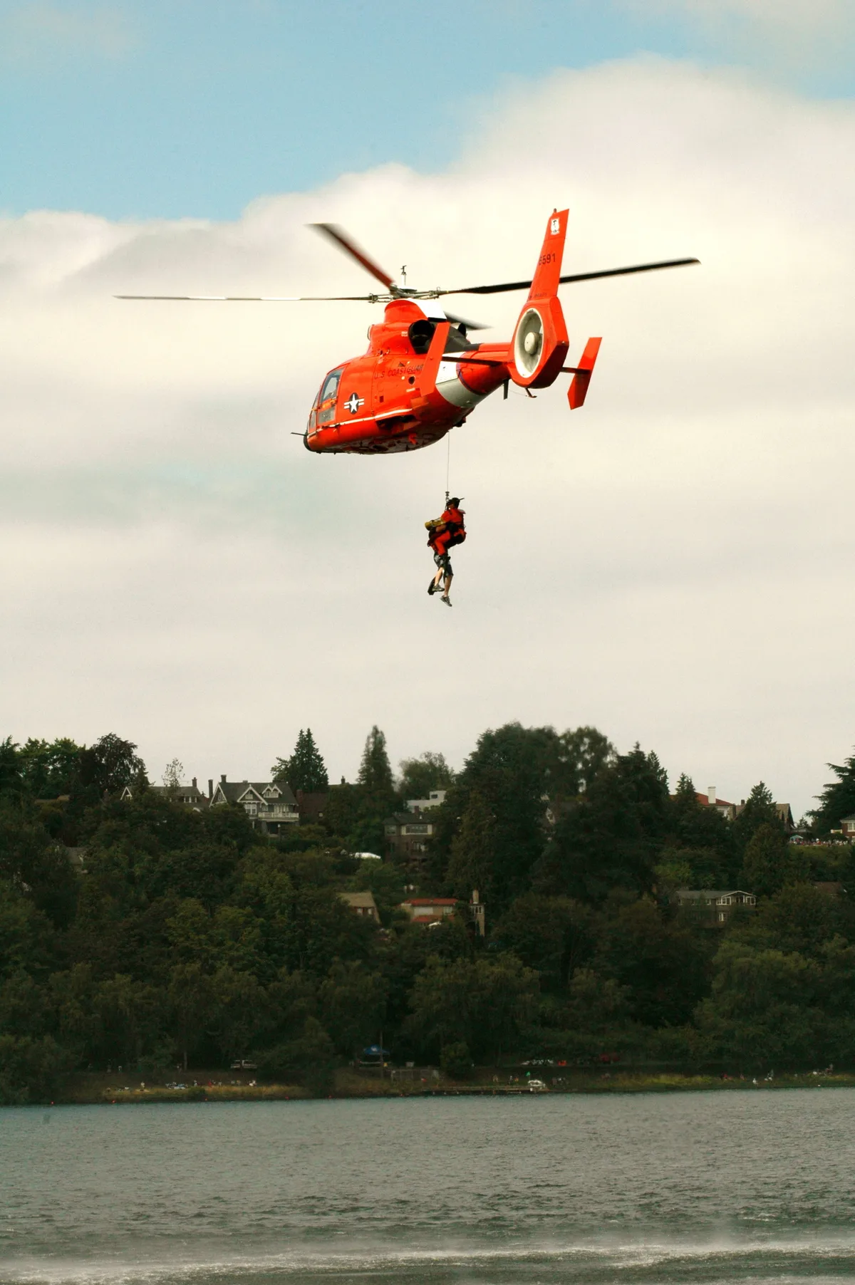 Coast Guard helicopter hoisting a rescue swimmer over the water